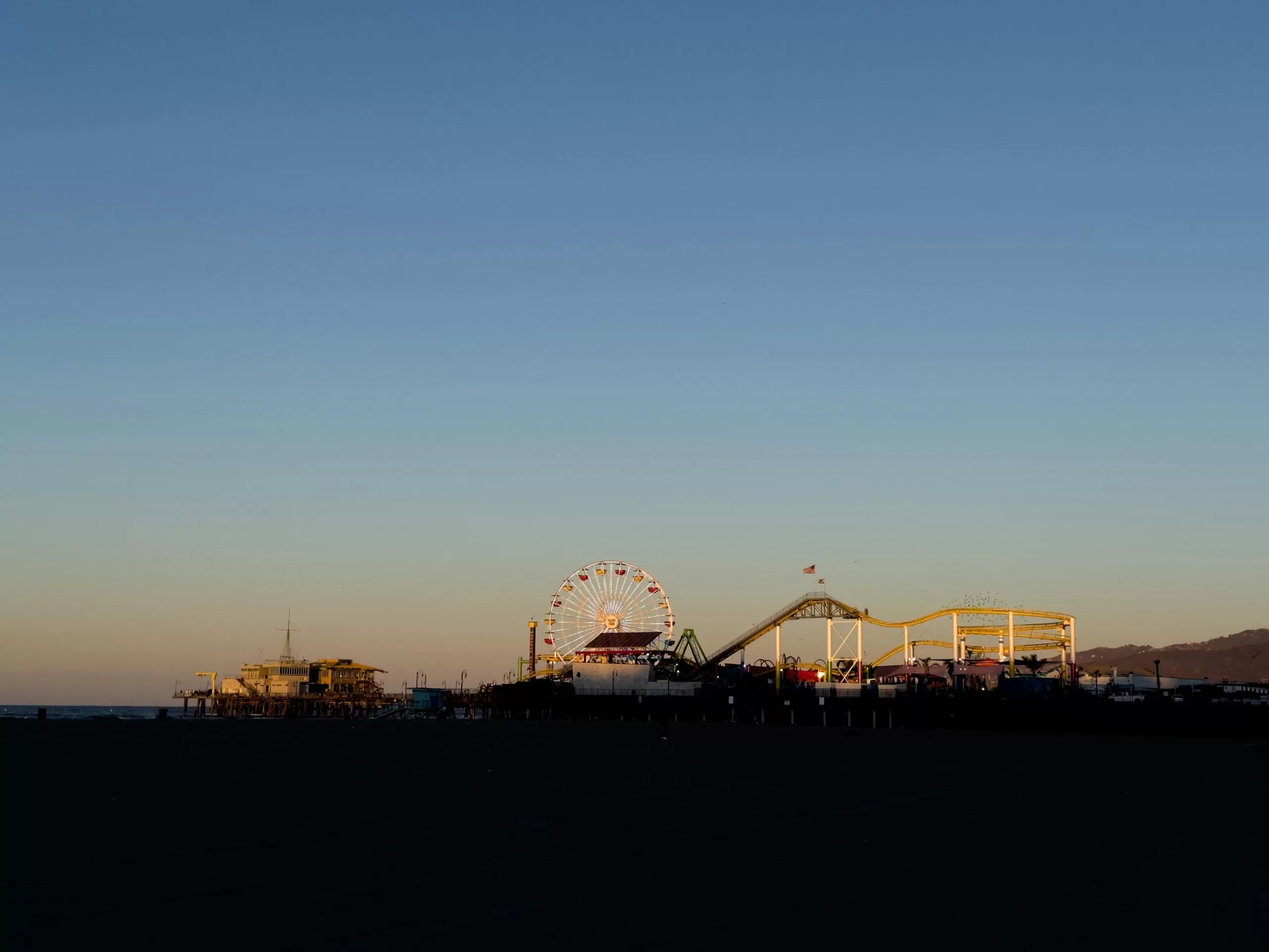 Santa Monica Pier silhouette at sunset with the Ferris wheel glowing, a magical end to a Los Angeles family vacation beach day
